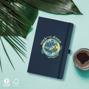 Notebook, journal on light blue background with palm leaves and coffee. Dark blue journal with a graphic that has a planet and the words Work Like You Give a Damn about People, Planet and Prosperity.